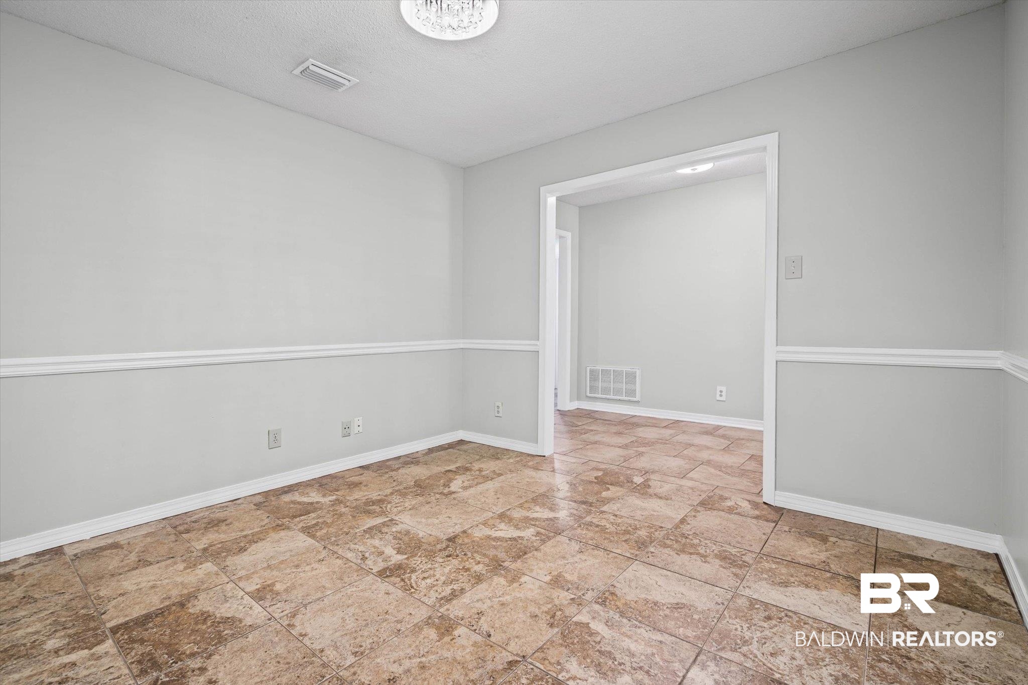 Empty room with mottled brown tile floors, gray walls, and a wide doorway to an adjoining room.