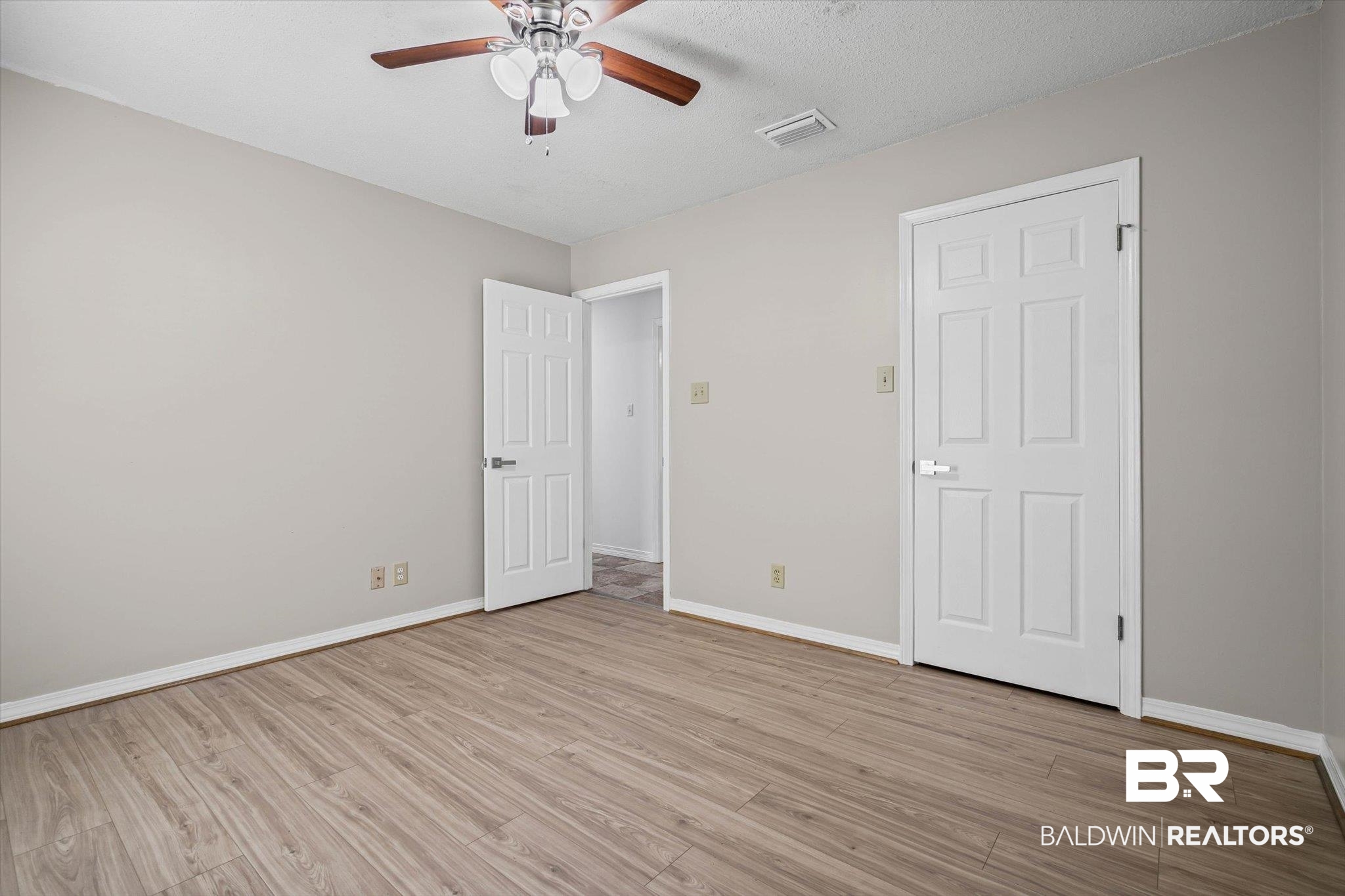 Empty bedroom with wood-look flooring, neutral walls, and a ceiling fan.