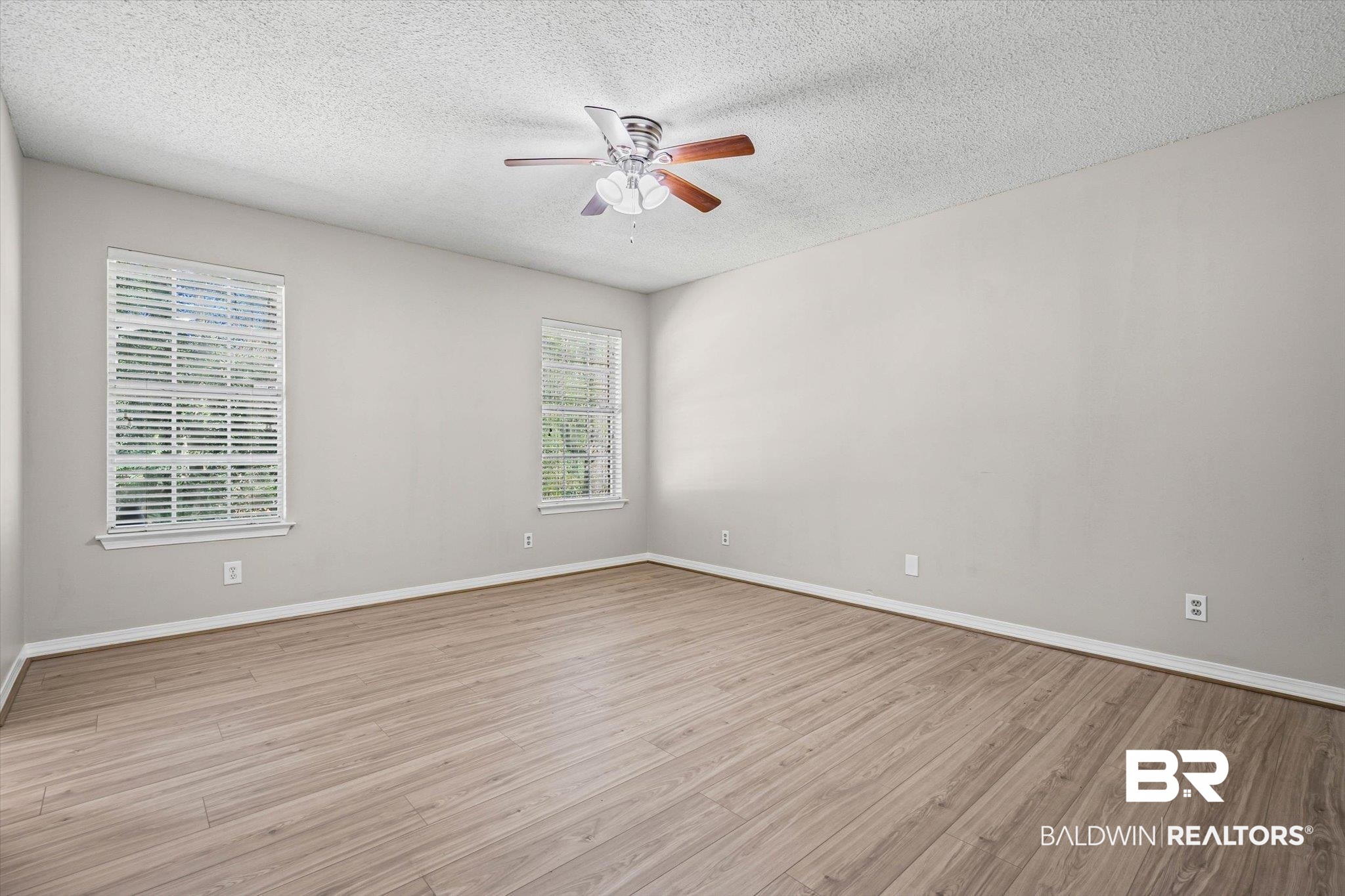Empty bedroom with wood-look flooring, two windows with blinds, and a ceiling fan.