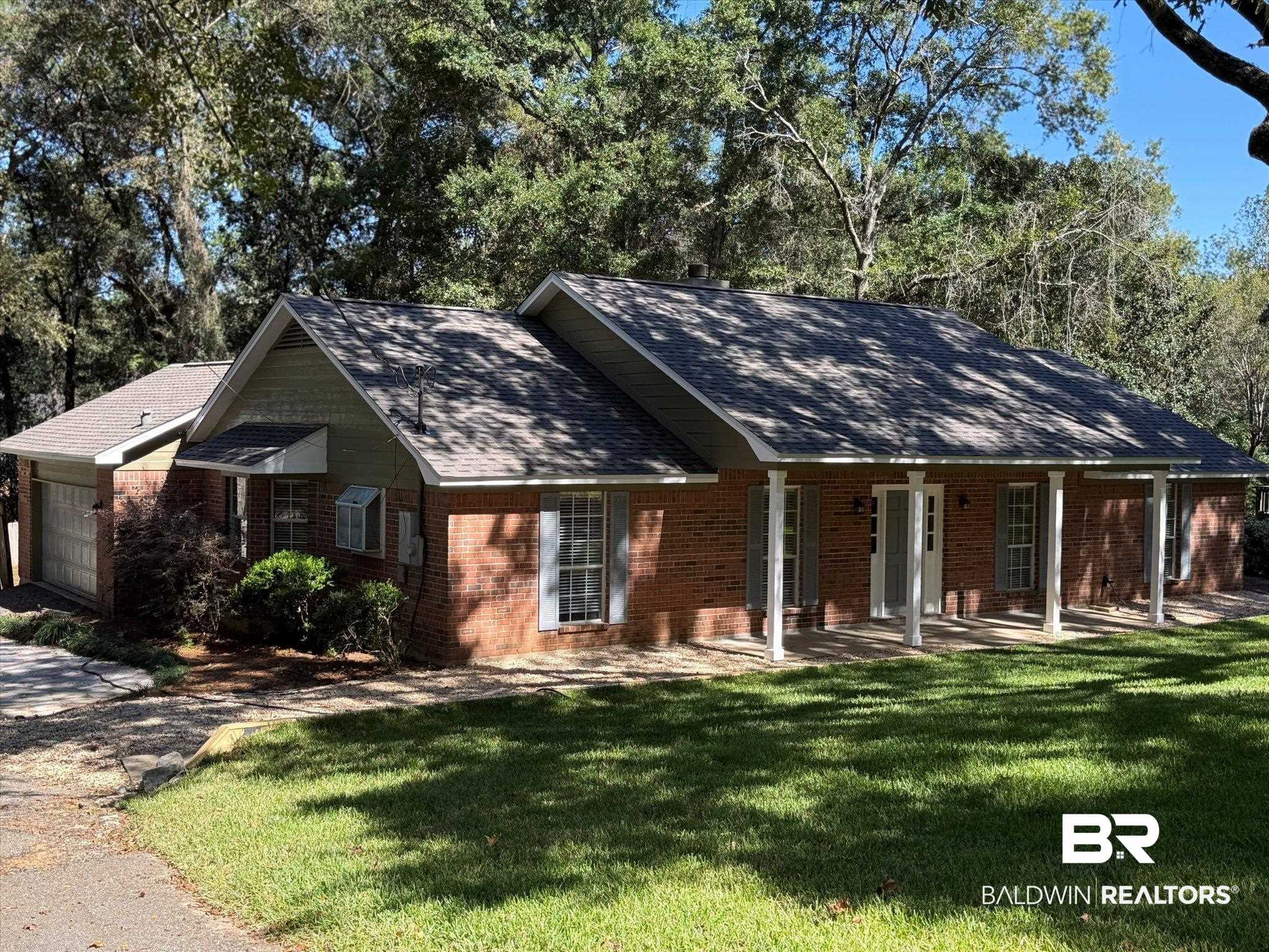 Red-brick single-story home with a covered front porch, attached garage, and shady lawn.