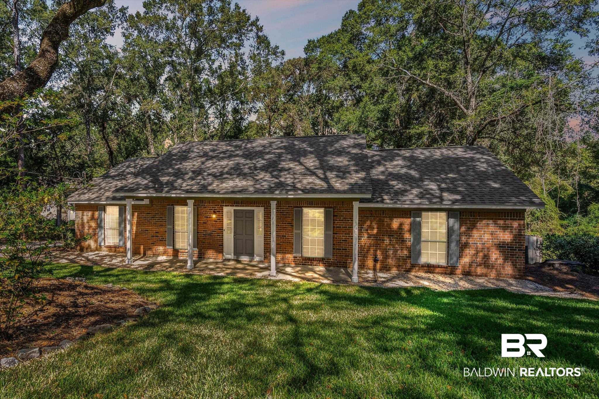 Single-story brick house with a covered porch, shaded by mature trees.