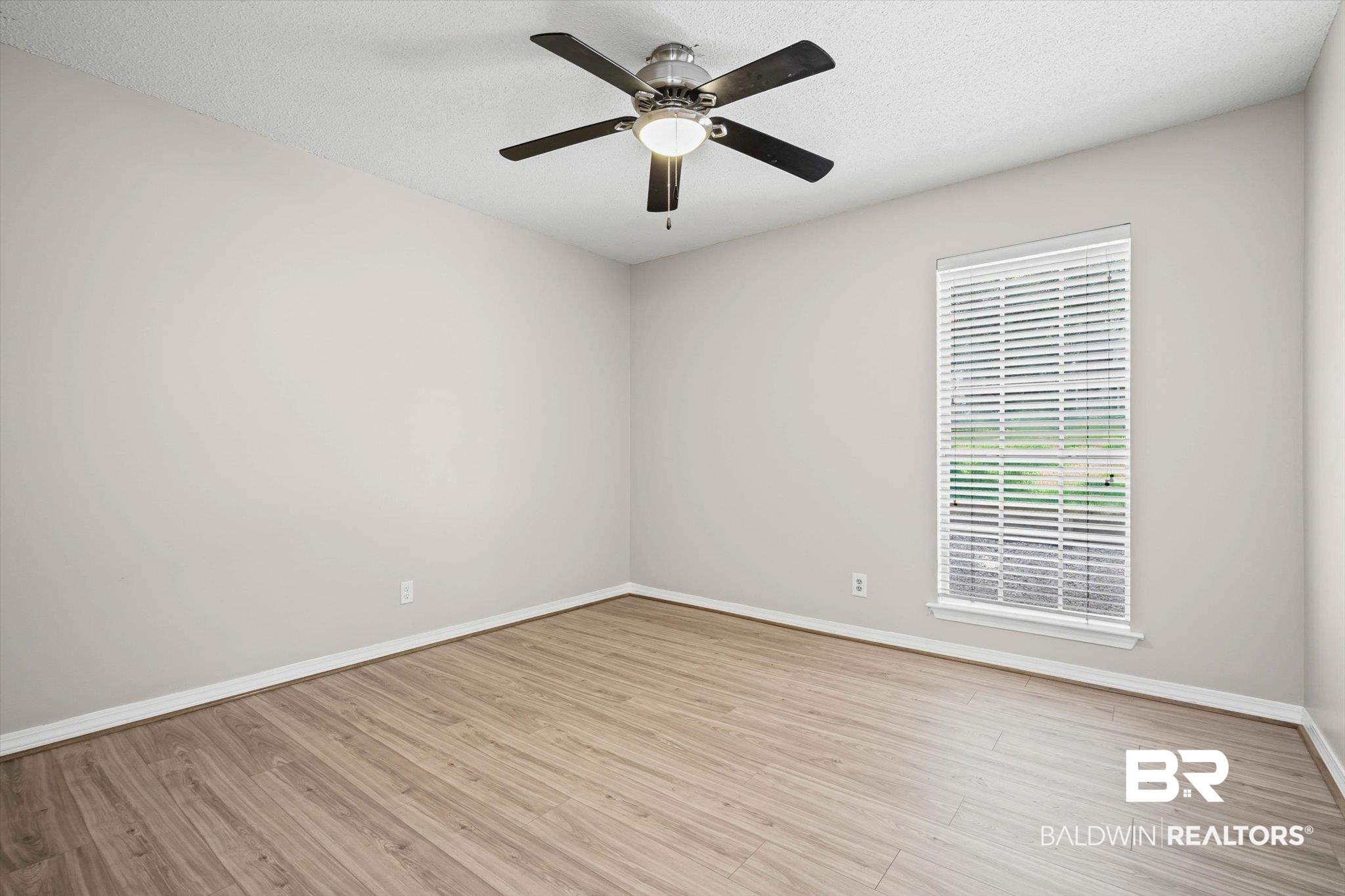 Empty room with light wood-look flooring, a ceiling fan, and a window with white blinds.