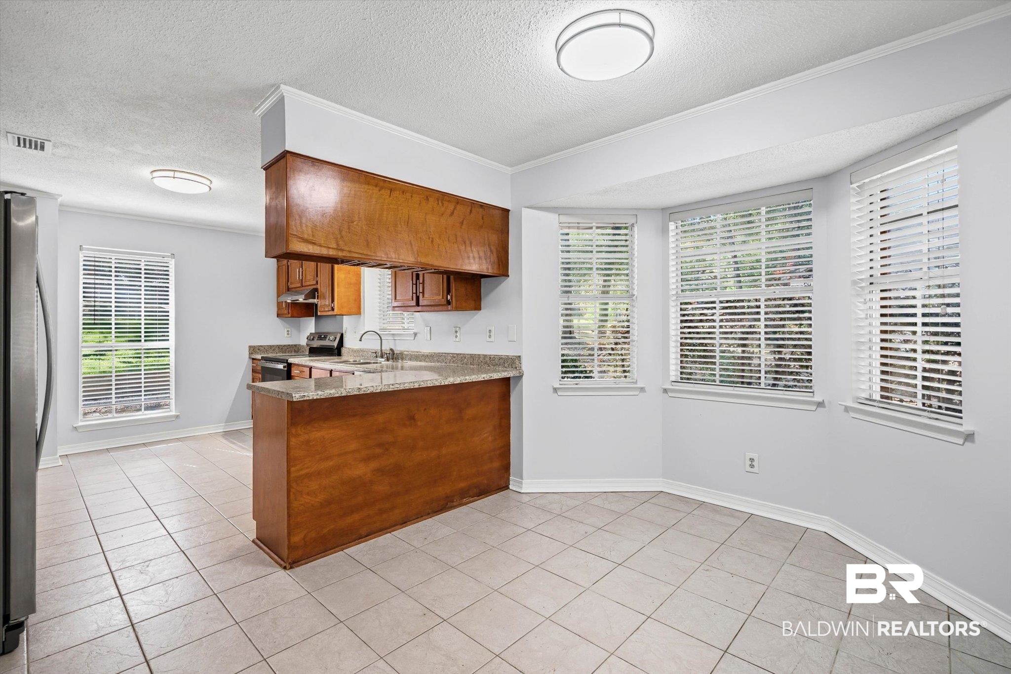 Vacant kitchen and dining area with warm wood cabinetry, a peninsula counter, and large windows with blinds.