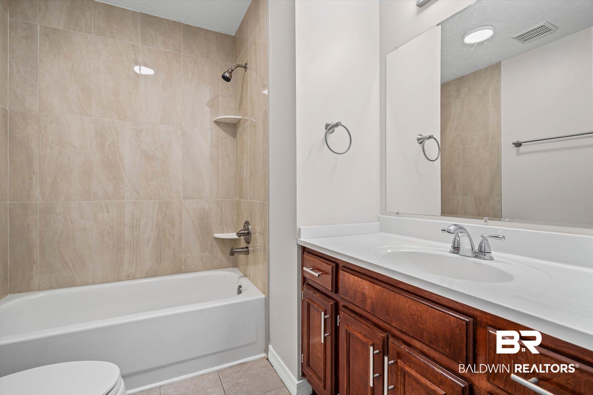 Bathroom with beige tiled tub surround, white sink countertop, and reddish-brown wood vanity.