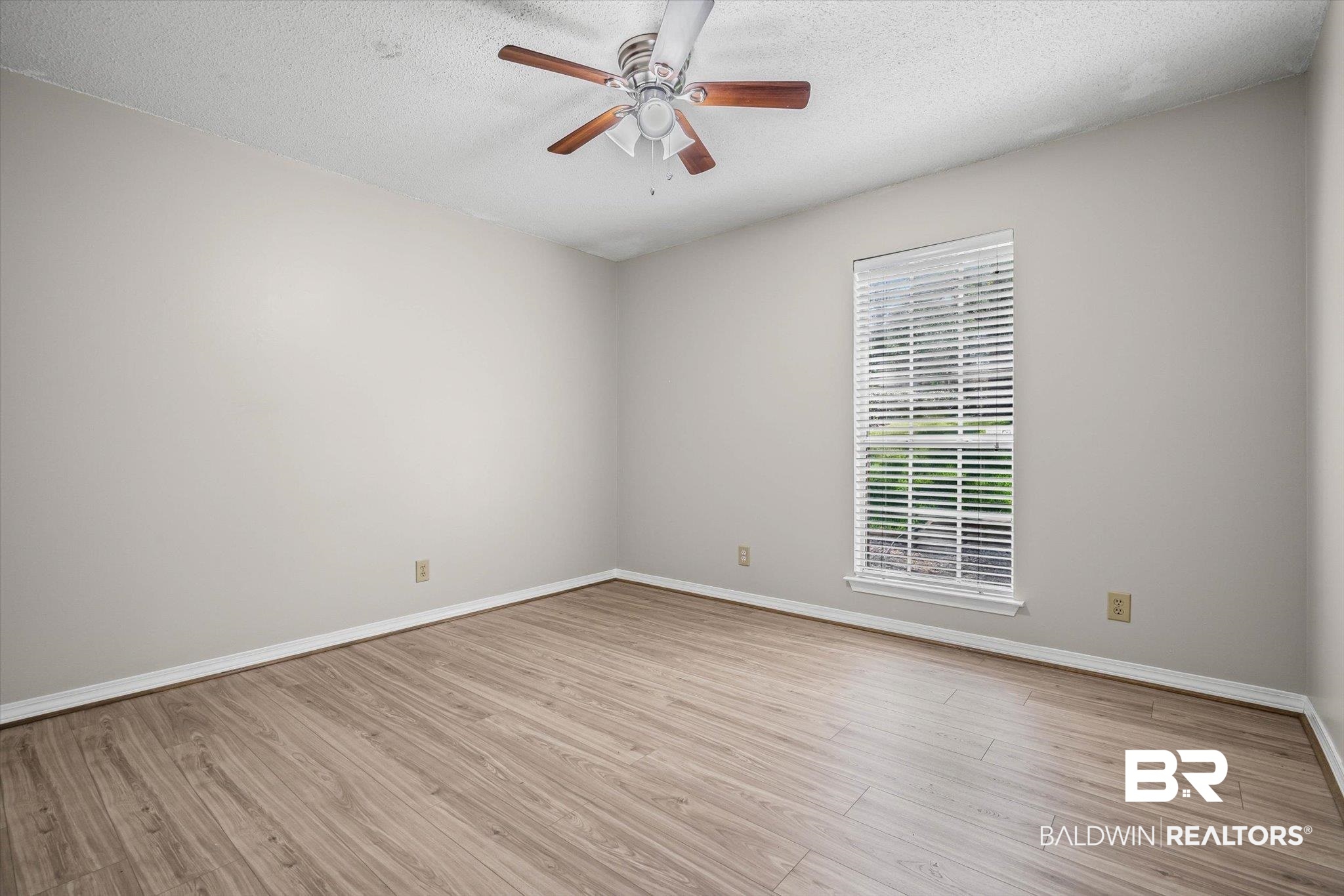 Empty room with wood-look flooring, a ceiling fan, and a window with blinds.