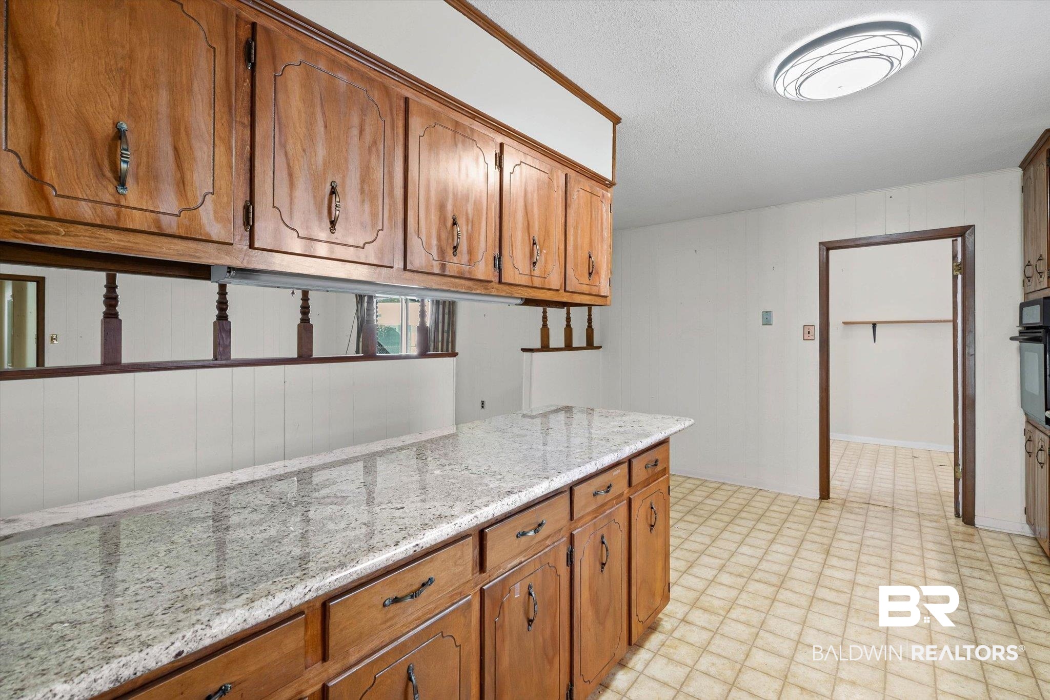 Kitchen with honey-toned wood cabinets, granite countertop, and tiled floor.
