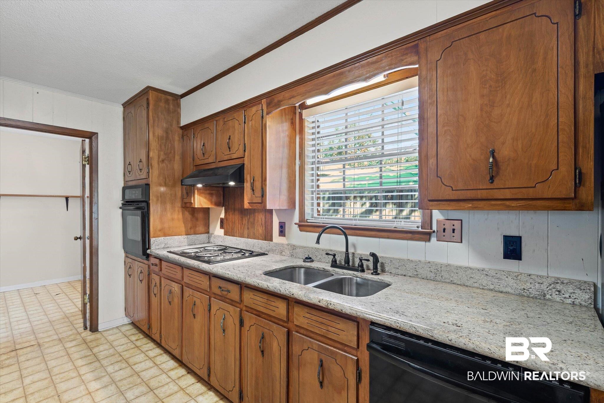Kitchen with warm wood cabinets, speckled countertops, and a double-basin sink beneath a window.