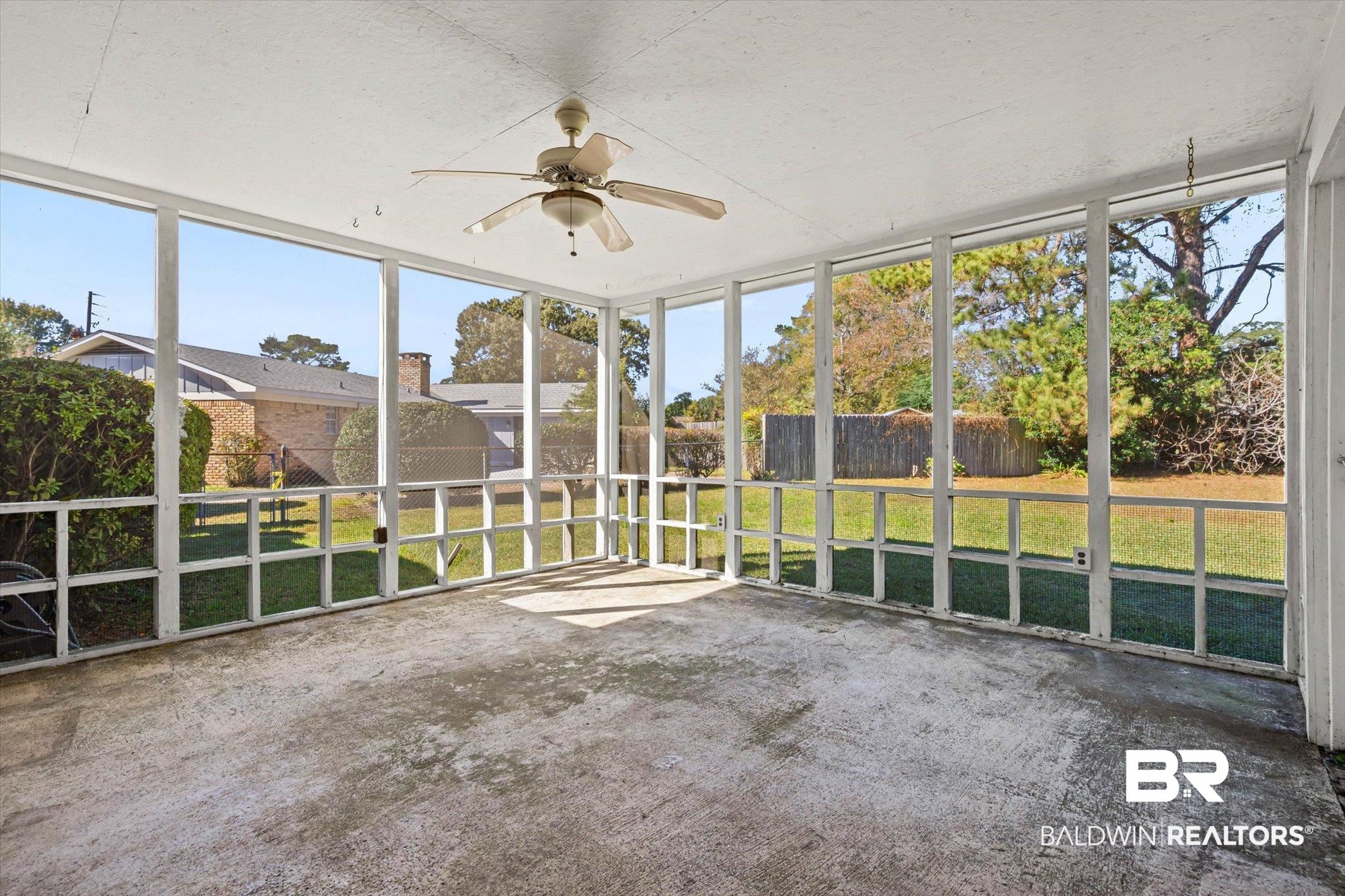 Screened-in back porch with a ceiling fan and views of the fenced backyard.