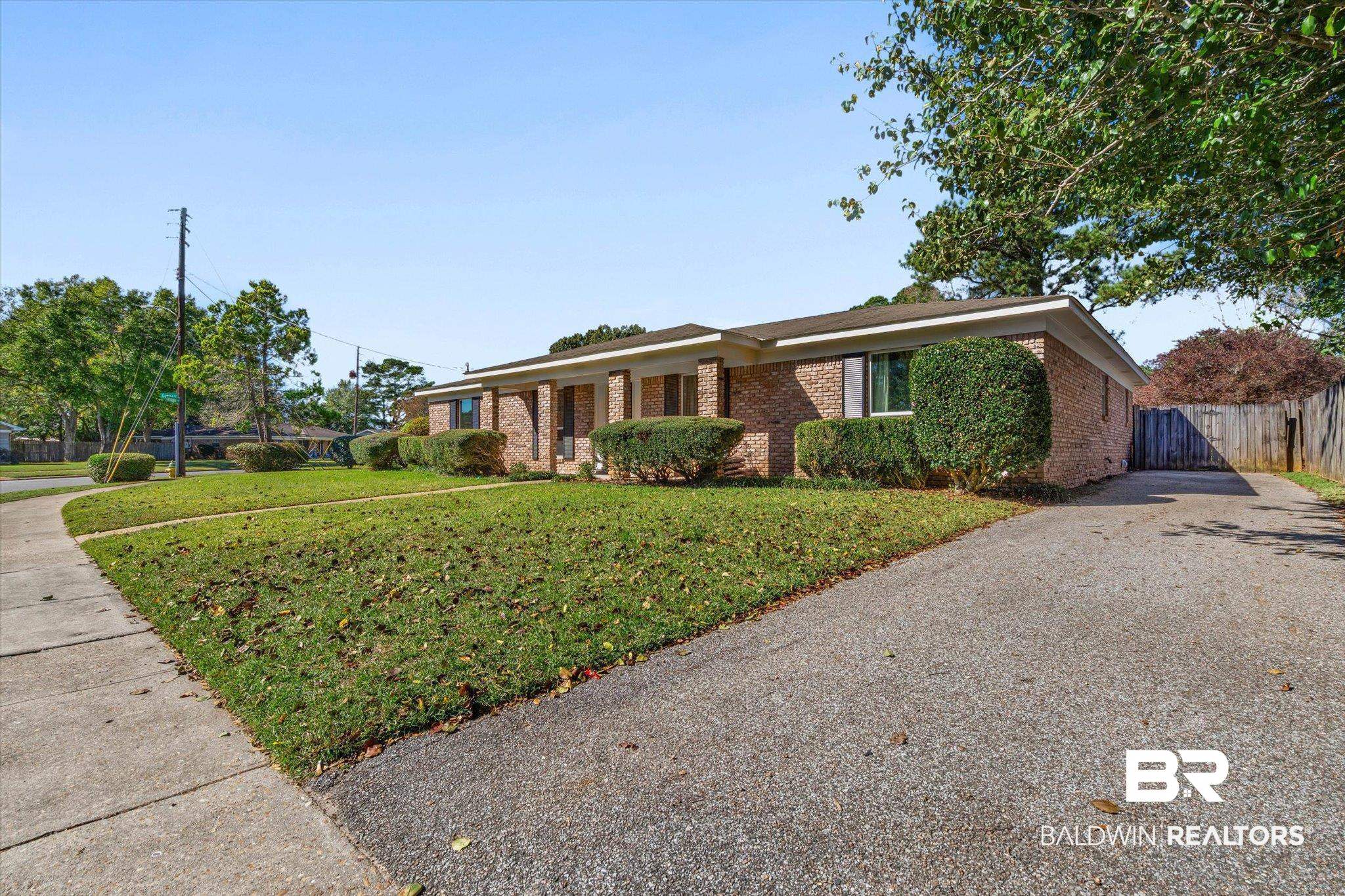 Single-story brick home with trimmed shrubs, front lawn, and broad paved driveway.