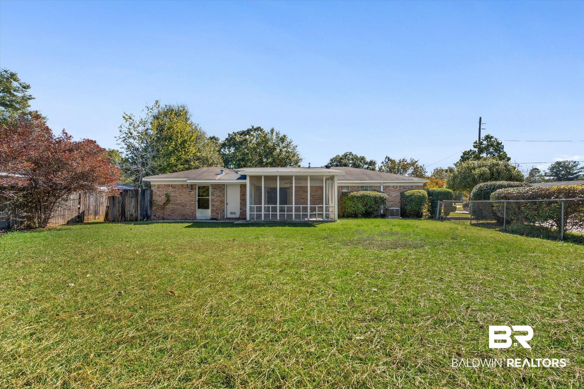 Single-story brick house viewed from the backyard, with a screened porch and a broad grassy lawn.