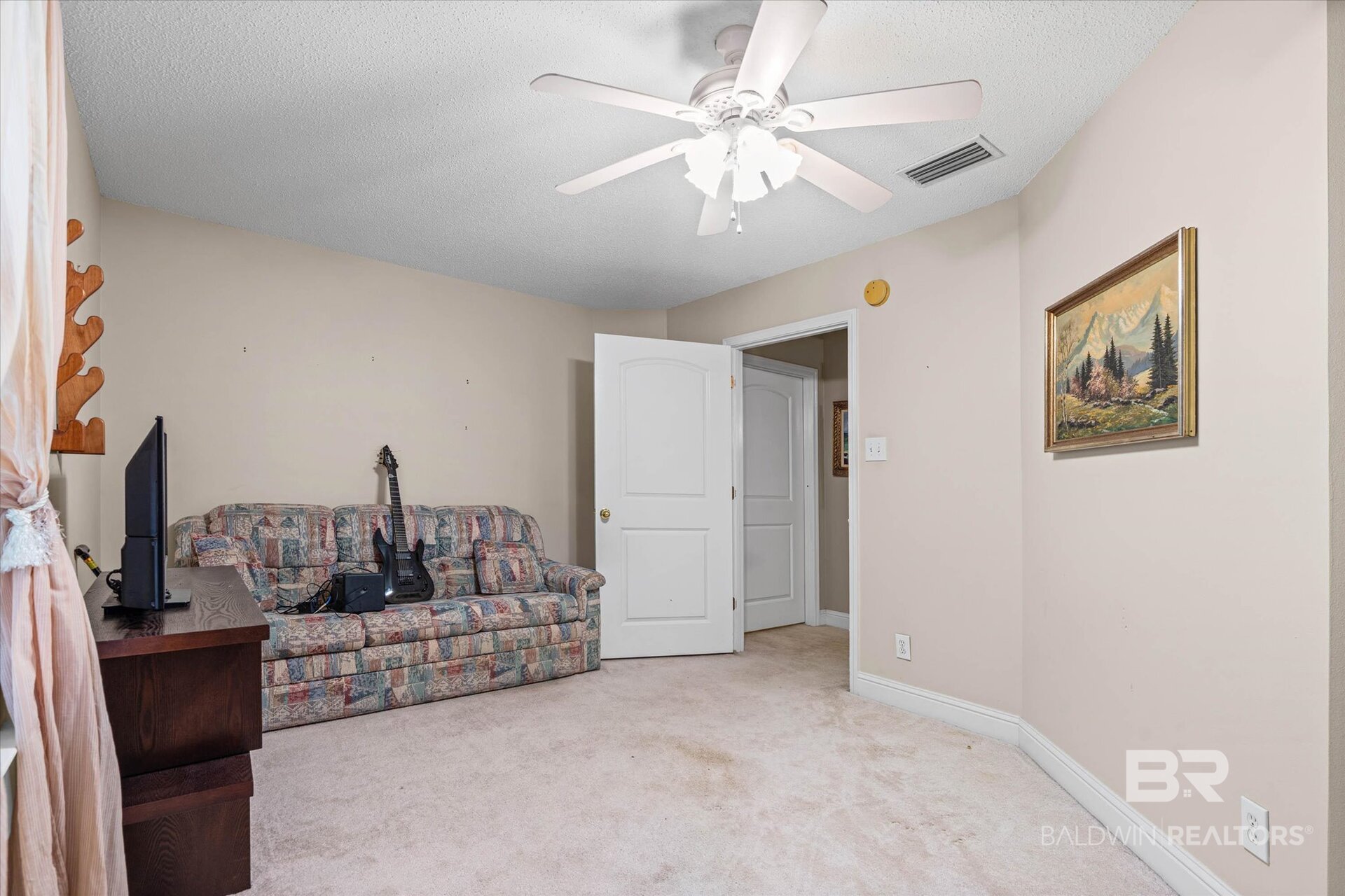 Living room with a patterned sofa, guitar, television, ceiling fan, and framed landscape painting.