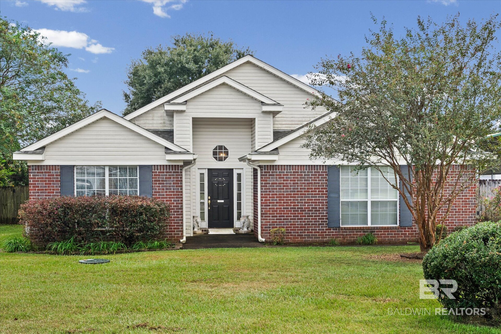 Brick and white-sided house with a black front door, blue shutters, and a broad lawn.