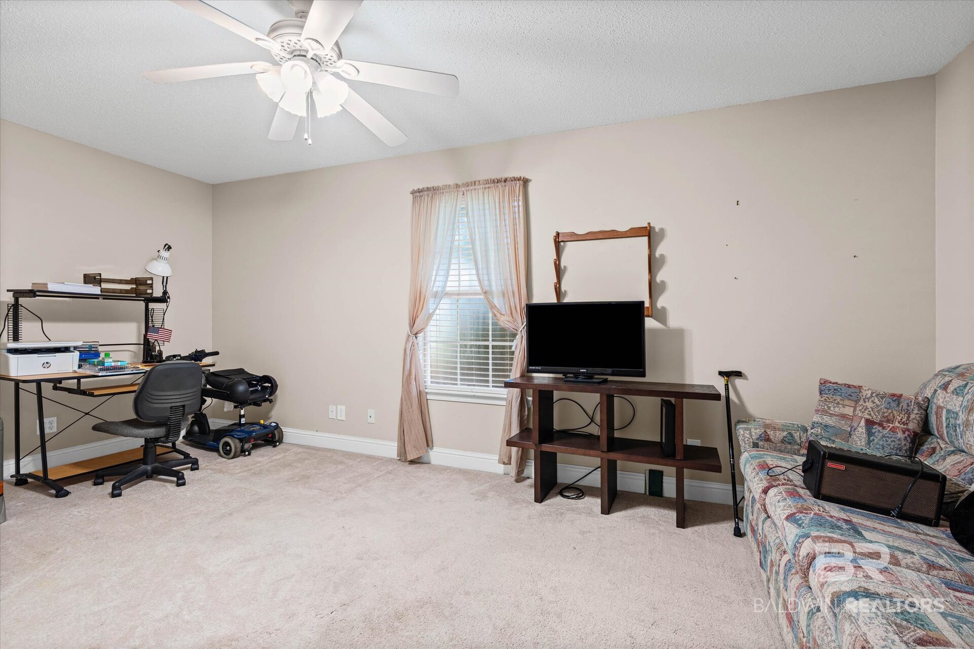 Furnished home office and sitting area with a desk, television, sofa, and curtained window.