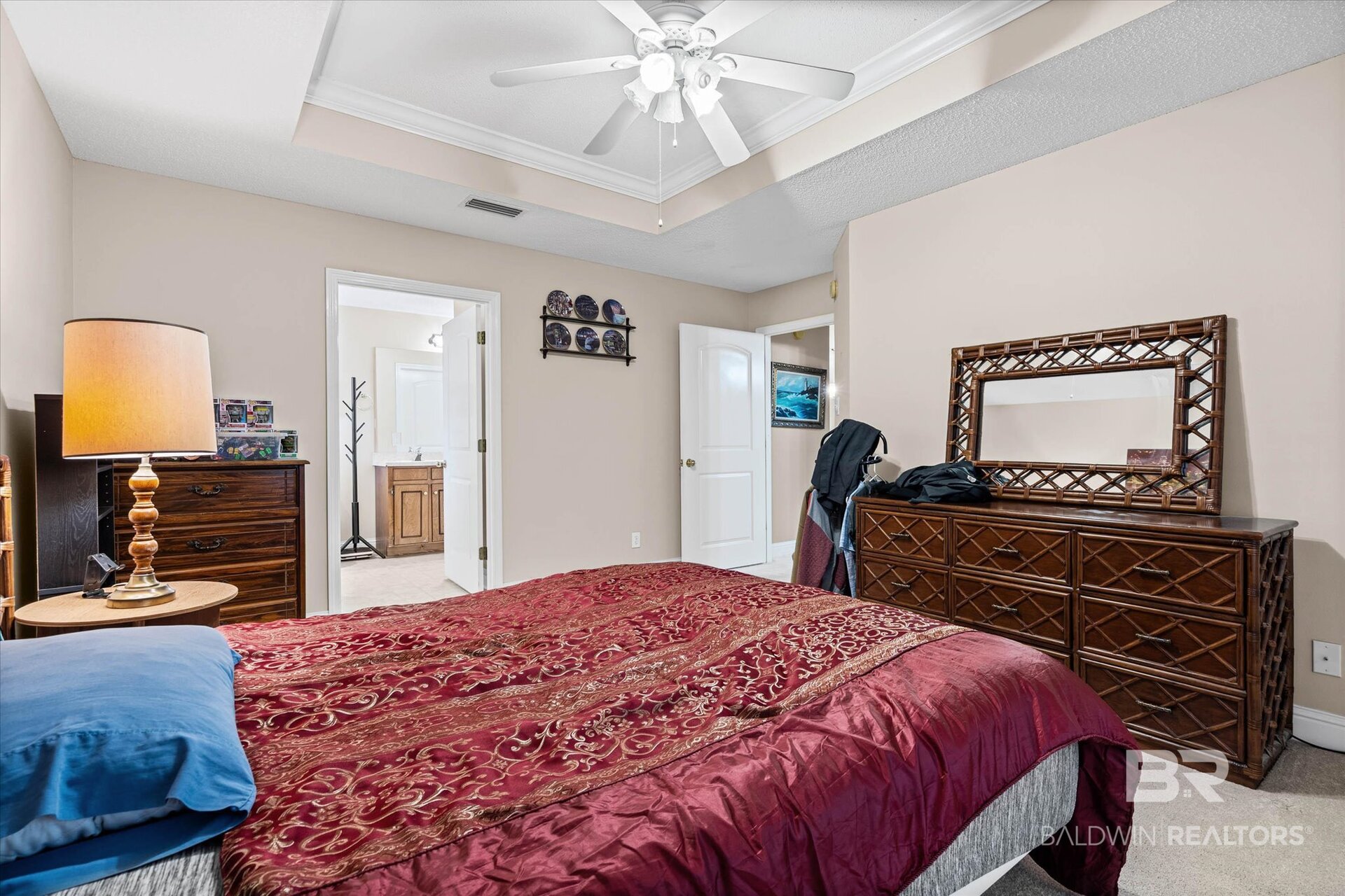 Bedroom with a red patterned bedspread, blue pillows, and dark wood dresser and mirror.