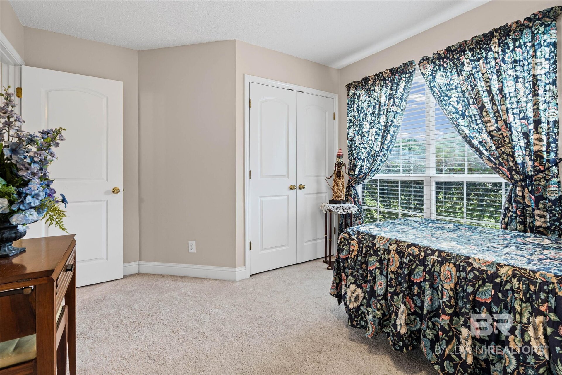 Bedroom with floral curtains and matching bedspread beside a large window.