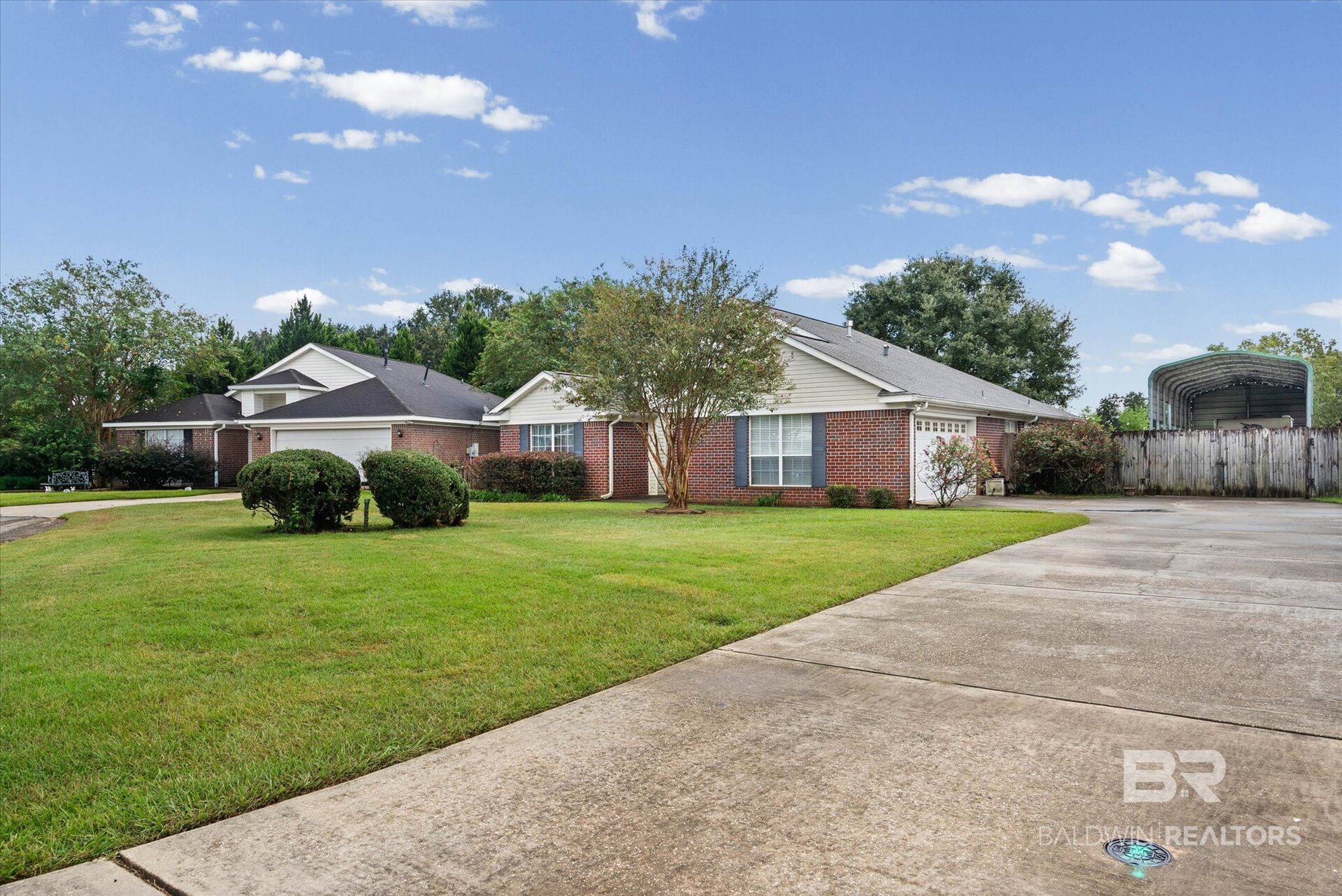 Single-story brick home with a broad driveway, landscaped lawn, and covered structure behind a fence.