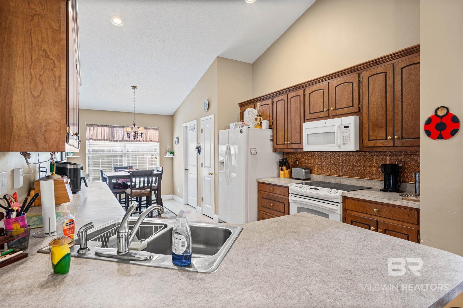 Kitchen with dark wood cabinets, stone counters, double-basin sink, and breakfast table by a large window.