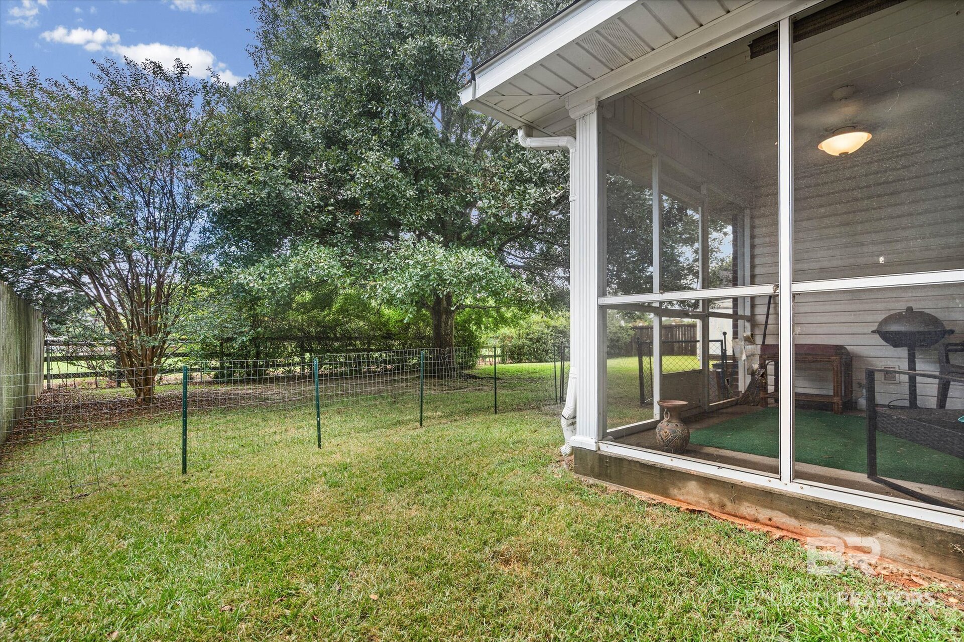 Fenced grassy backyard beside a screened porch, shaded by mature trees.