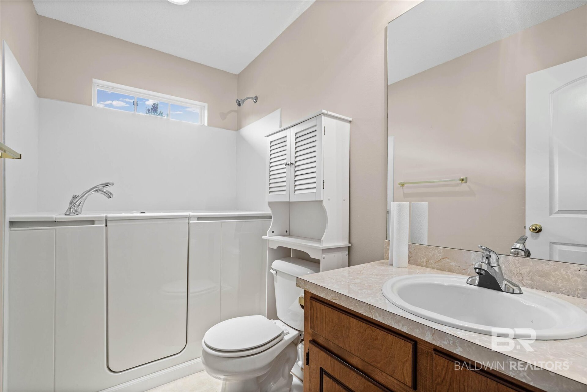 Bathroom with white tub and shower enclosure, toilet, louvered cabinet, and wood vanity.
