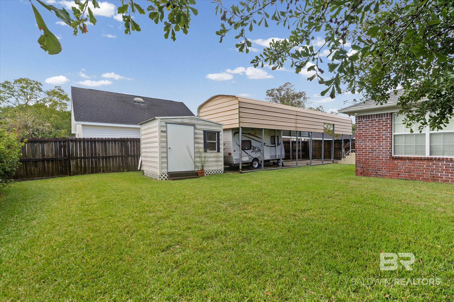 Backyard with a small storage shed and an RV parked beneath a long covered shelter.