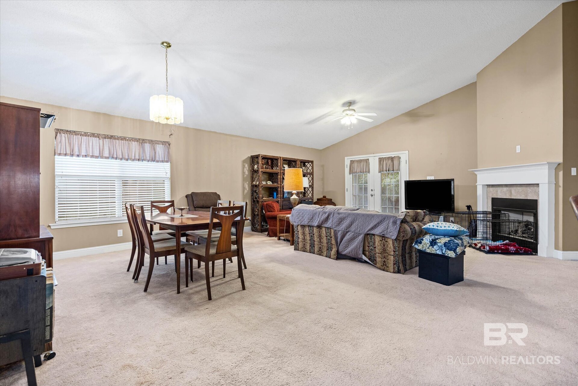 Open living and dining room with a carpeted floor, wooden dining set, sofa, and white fireplace.