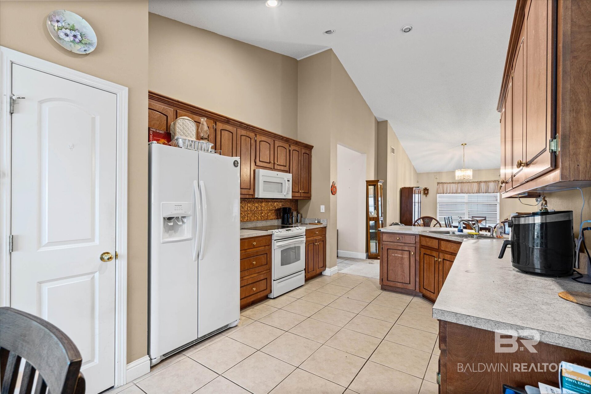 Kitchen with dark wood cabinetry, a central island, and white appliances, opening to a dining area.
