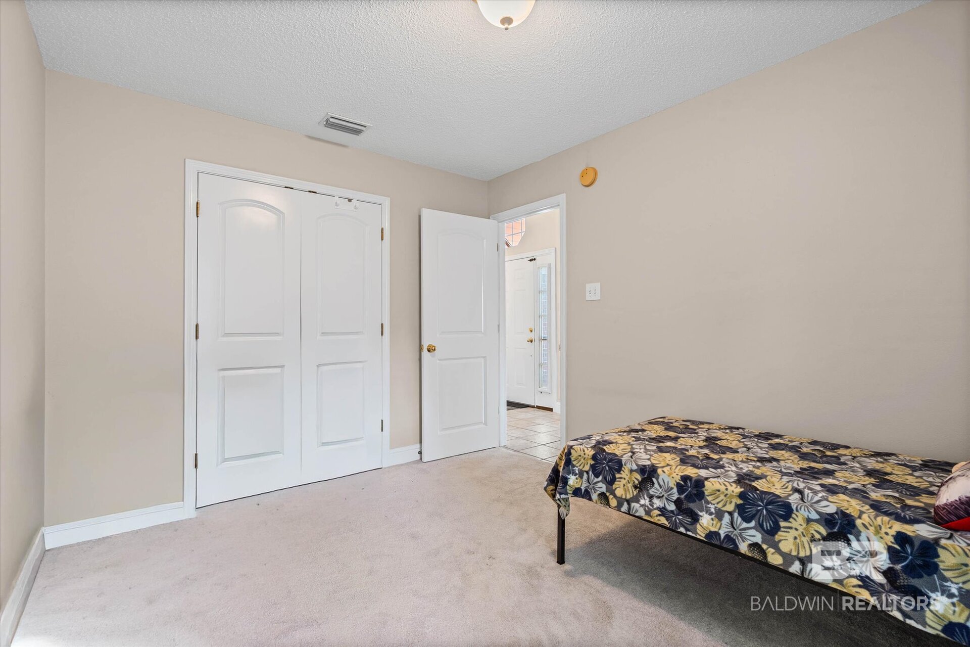 Bedroom with white double closet doors, light carpet, and a bed covered in a dark floral quilt.