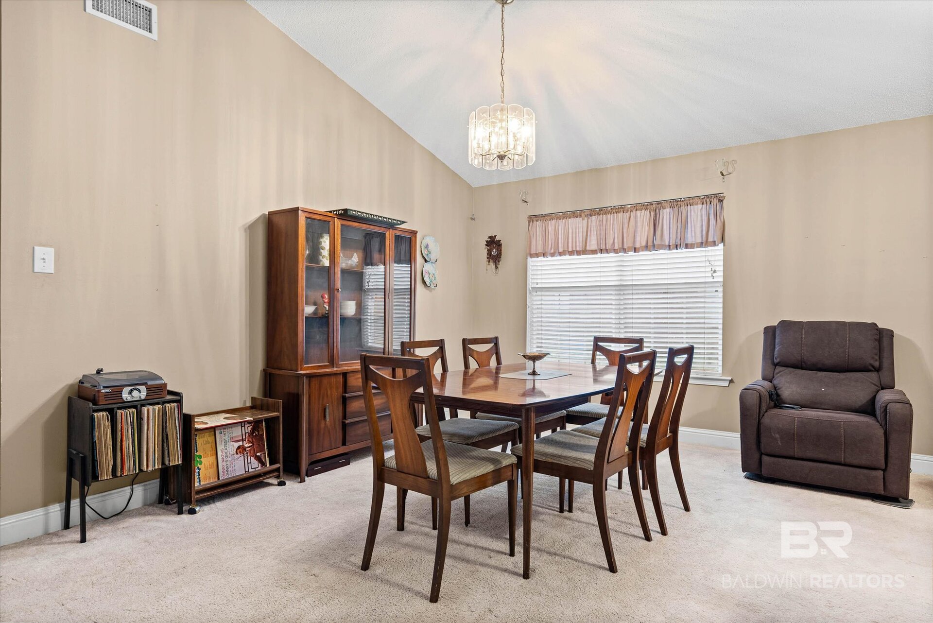 Dining room with a dark wood table, glass-front china cabinet, and large window with blinds.