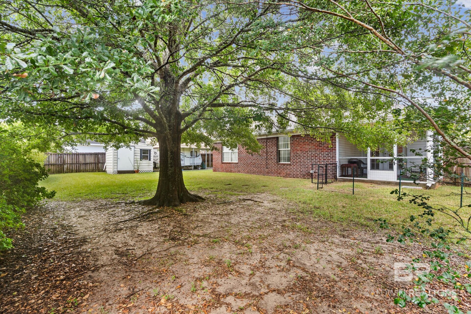 Brick home’s backyard with a large shade tree, lawn, and screened porch.
