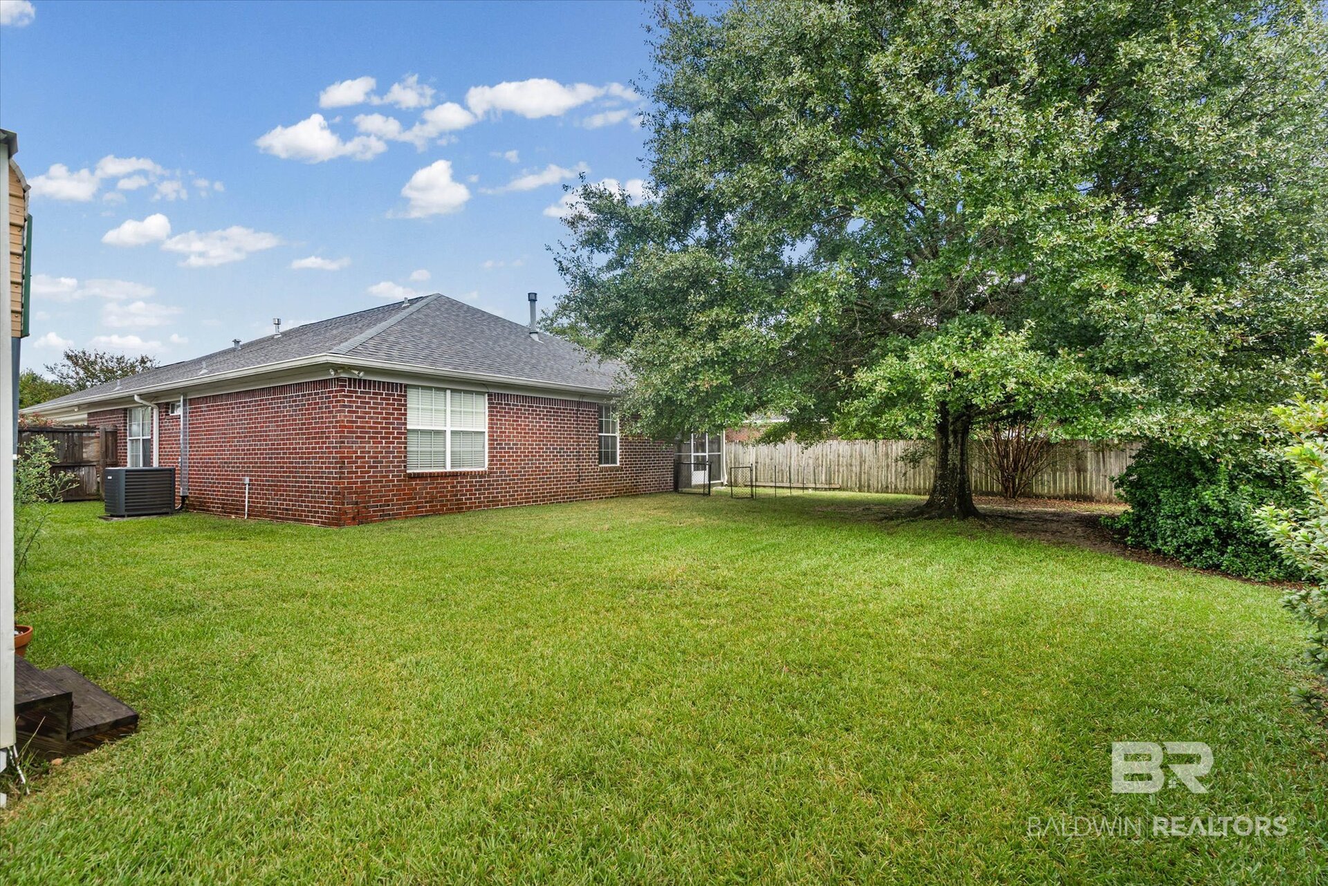 Fenced backyard with a broad lawn, red brick house, and large shade tree.