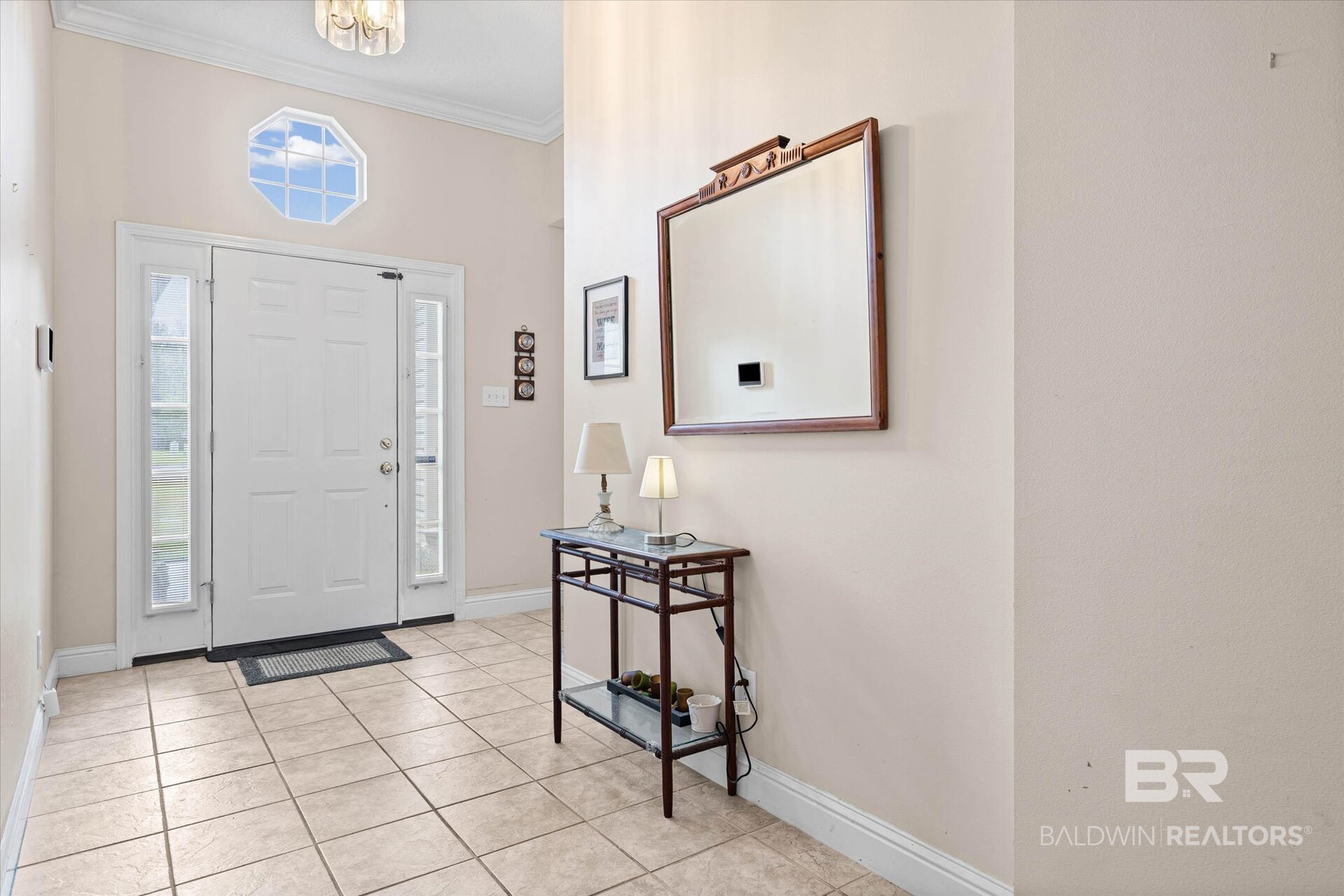 Entry foyer with tiled floor, white front door, octagonal window, and console table beneath a large mirror.