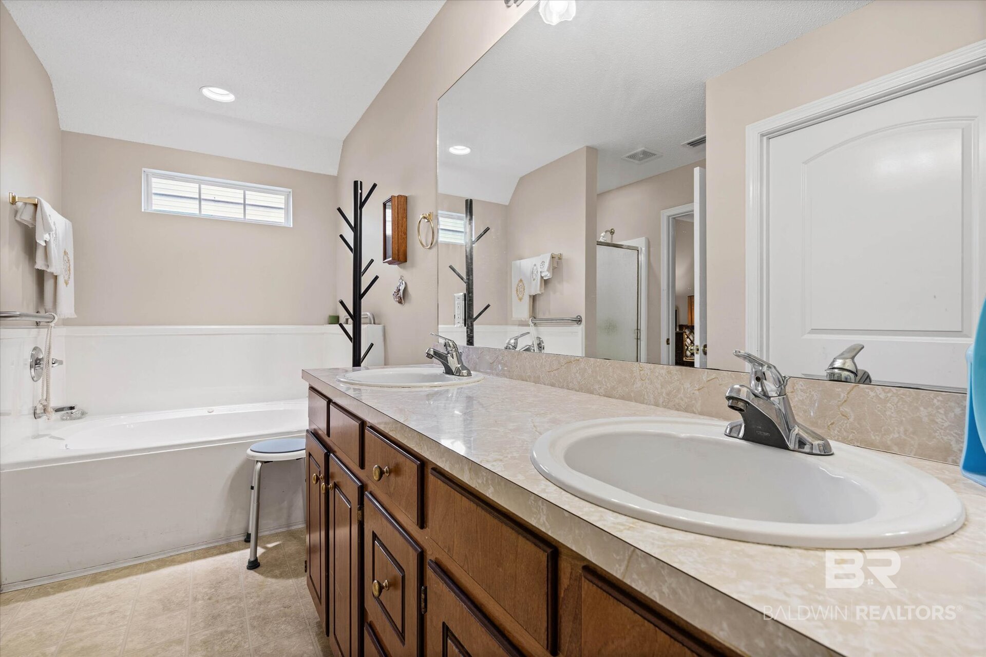 Bathroom with a double-sink wood vanity, large mirror, and white bathtub with shower.