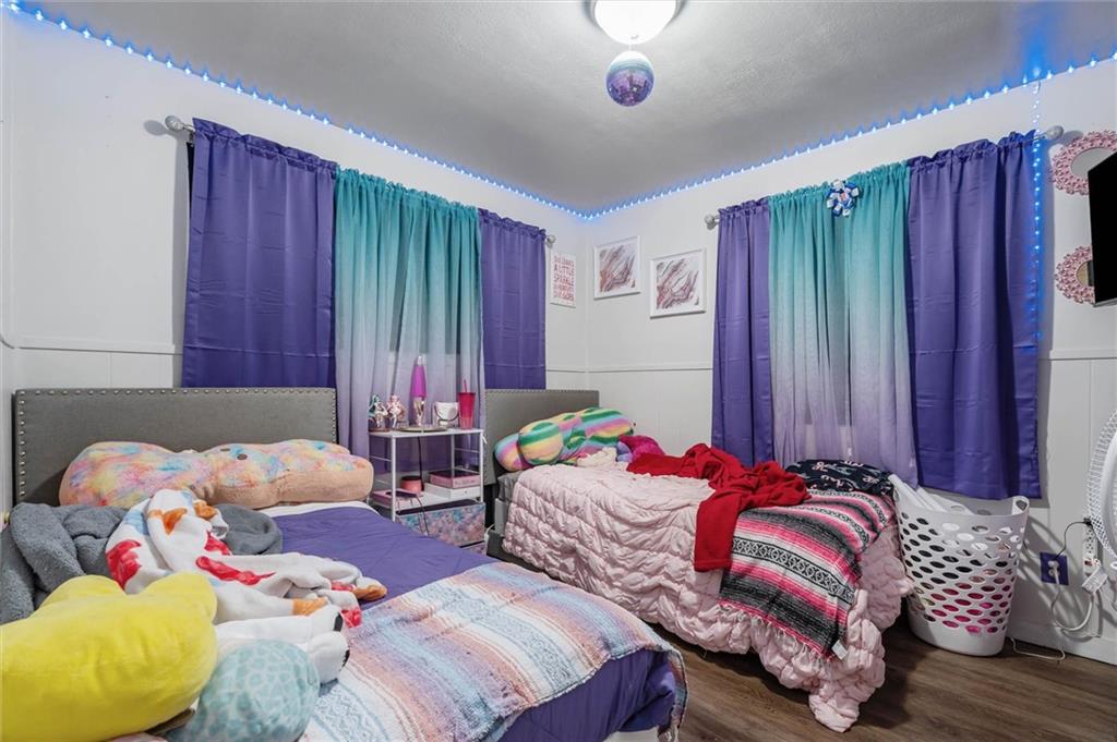 Bedroom with two beds, colorful bedding, purple and teal curtains, and blue ceiling lights.