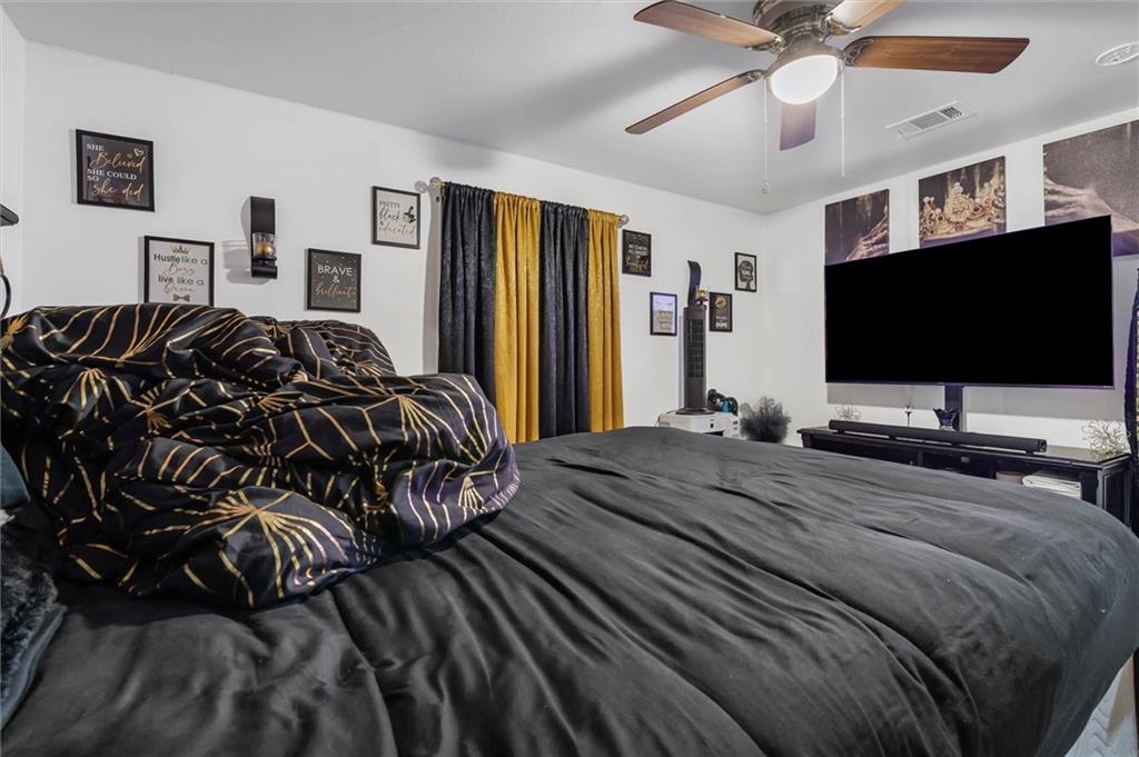 Furnished bedroom with dark bedding, a black-and-gold comforter, and a large television.