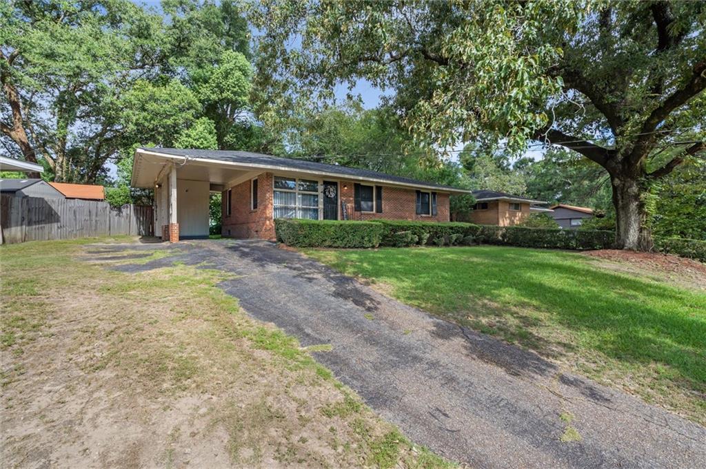 Single-story brick house with a covered carport, wide driveway, and mature shade trees.