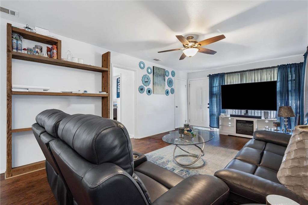 Living room with dark leather seating, built-in wooden shelves, and blue curtains framing a large window.