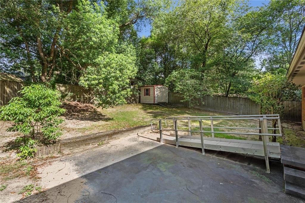 Fenced backyard with mature trees, a storage shed, and a metal accessibility ramp.