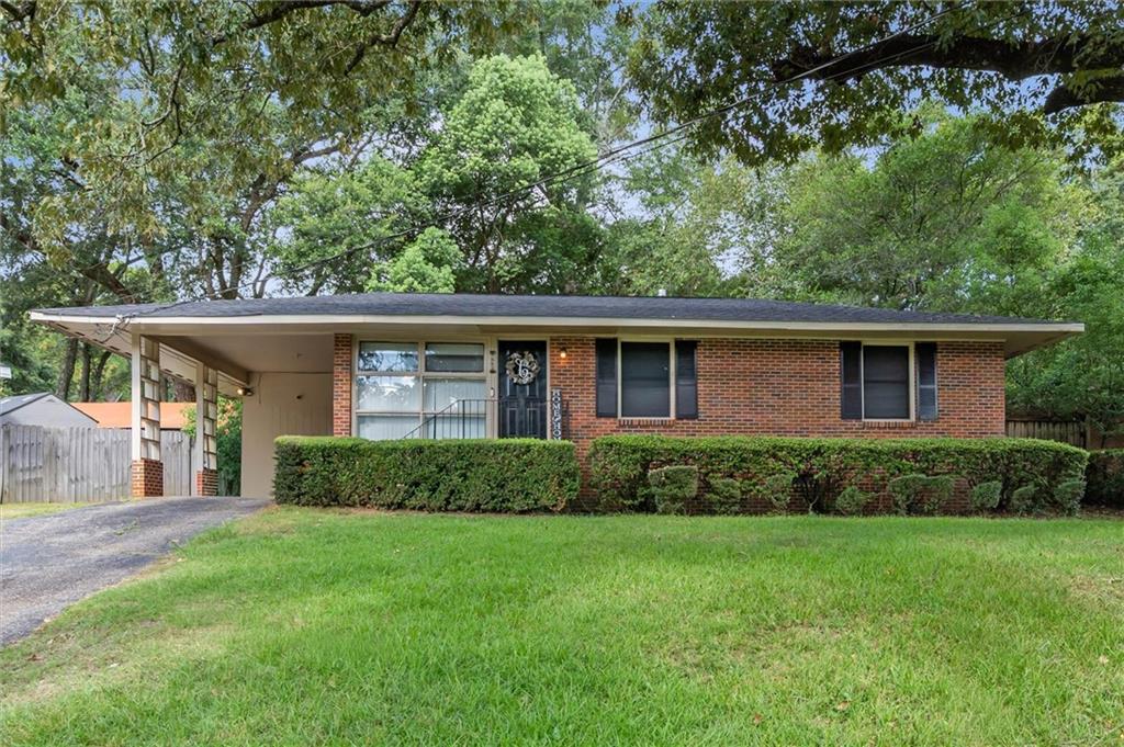 Single-story brick house with a covered carport, trimmed hedges, and a broad front lawn.