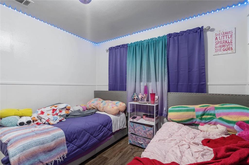 Bedroom with two beds, purple and teal curtains, and blue lights along the ceiling.