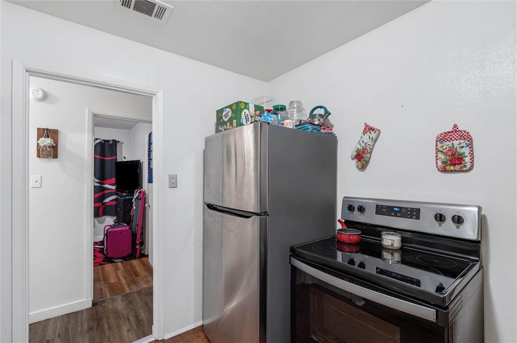 Compact kitchen with a stainless-steel refrigerator and black glass-top range beside an open doorway.
