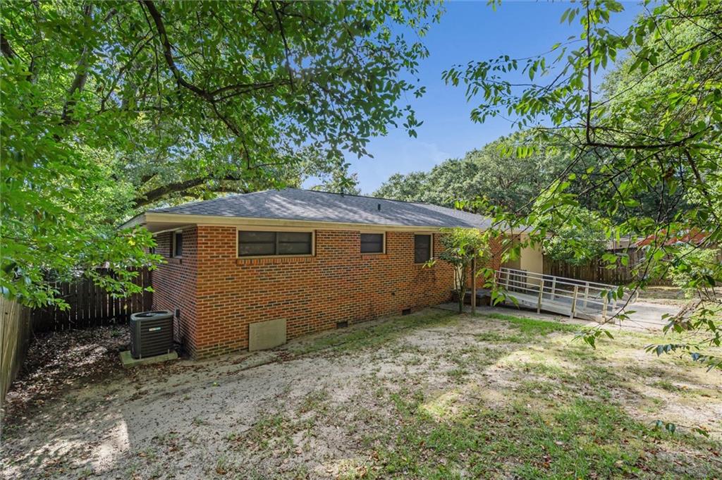 Single-story brick home with an accessibility ramp and mature trees shading the sandy yard.