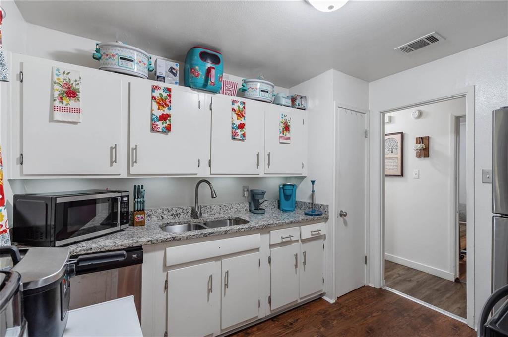 Kitchen with white cabinets, granite countertops, a stainless steel sink, and dark wood flooring.