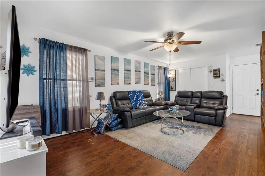 Living room with black leather sectional sofas, a glass coffee table, and hardwood floors.