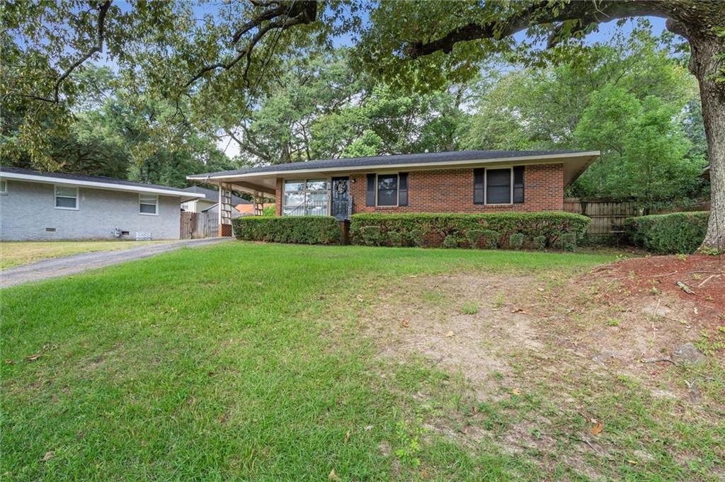 Brick ranch house with a covered carport, grassy front yard, and mature trees.