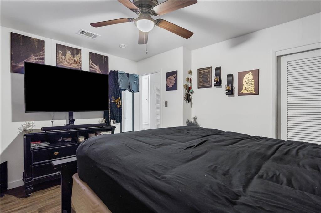 Bedroom with a large dark-covered bed, ceiling fan, and television above a black dresser.