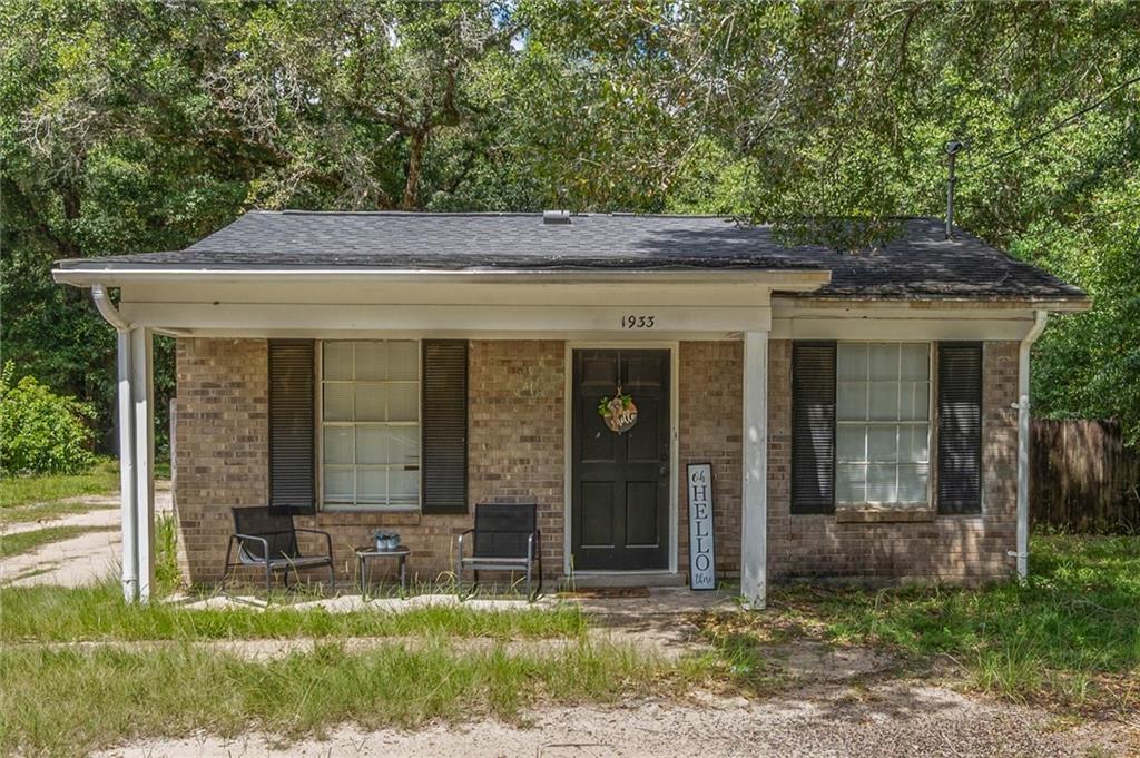 Single-story brick house with a covered porch, black front door, and mature trees.
