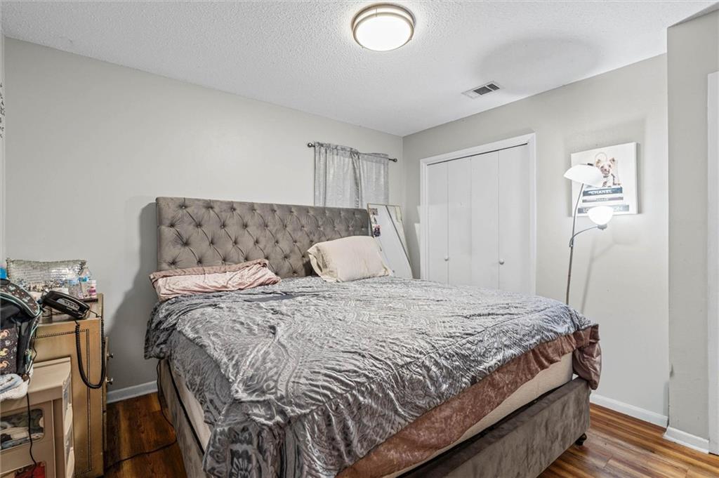 Furnished bedroom with a large tufted bed, patterned bedding, hardwood floors, and a sliding-door closet.