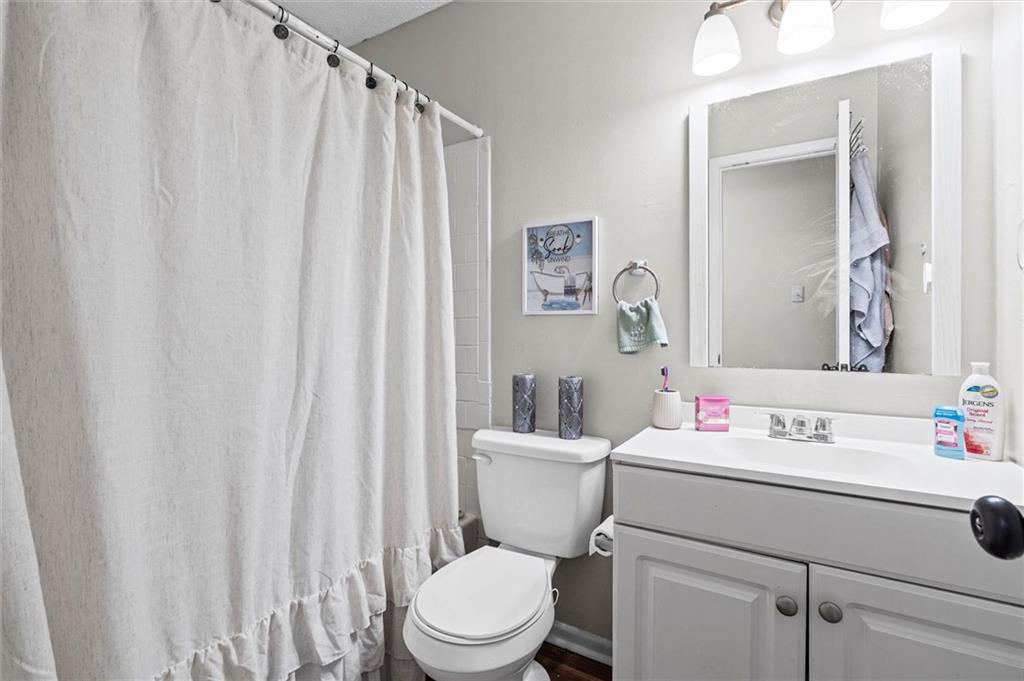 Bathroom with a white shower curtain, toilet, and vanity beneath a large mirror.