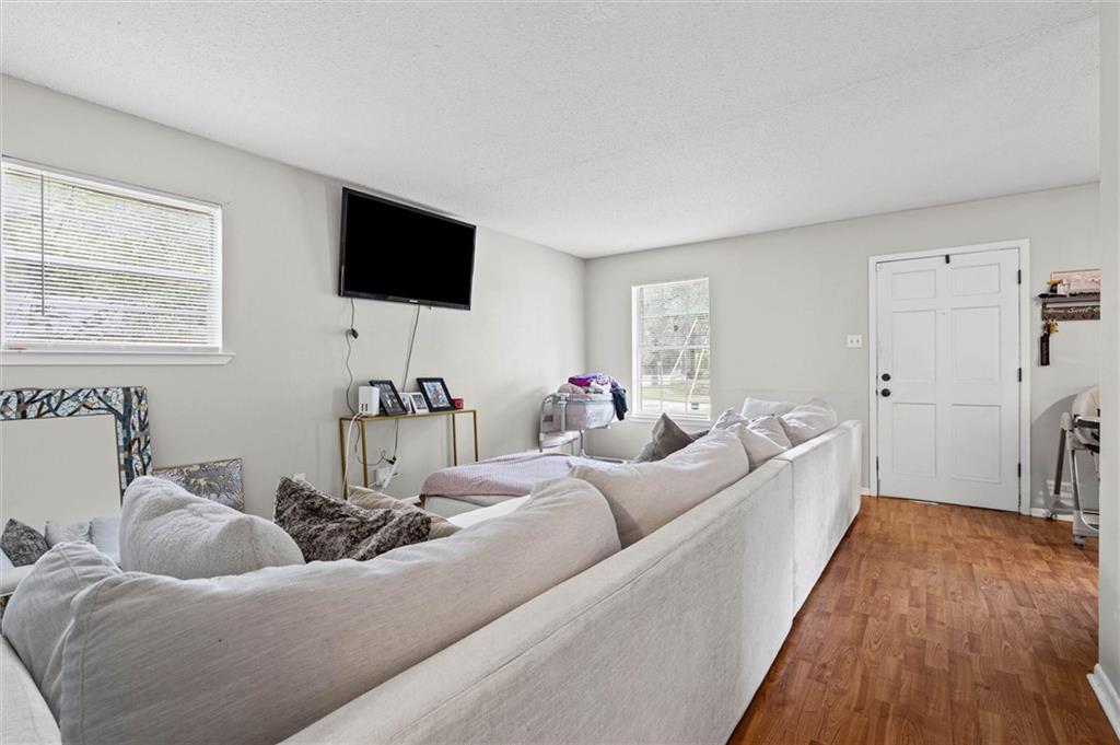 Living room with a large white sectional sofa, wood-look flooring, and wall-mounted television.
