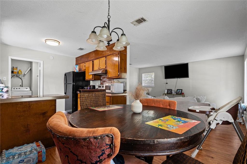 Open-plan dining and kitchen area with a round dark wood table, wood cabinets, and a laundry nook.